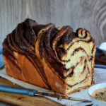 Close-up of a marbled chocolate swirl loaf cake on a wooden cutting board with a blue-handled knife nearby.